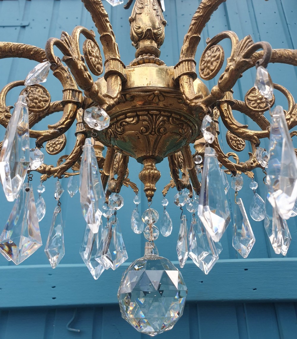 An eight-arm French gilt brass chandelier decorated with scrolling foliate detail, faux candle sleeves, and faceted hanging cut-glass crystal drops. View V