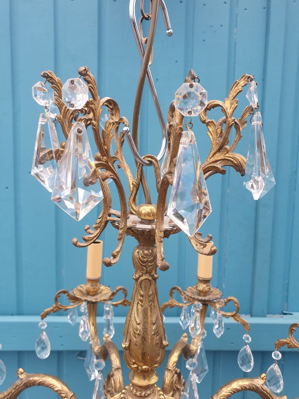An eight-arm French gilt brass chandelier decorated with scrolling foliate detail, faux candle sleeves, and faceted hanging cut-glass crystal drops. View VI