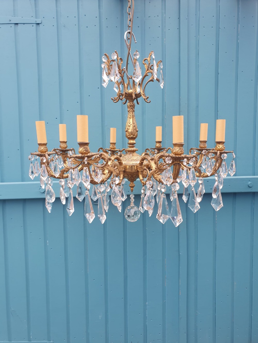 An eight-arm French gilt brass chandelier decorated with scrolling foliate detail, faux candle sleeves, and faceted hanging cut-glass crystal drops.