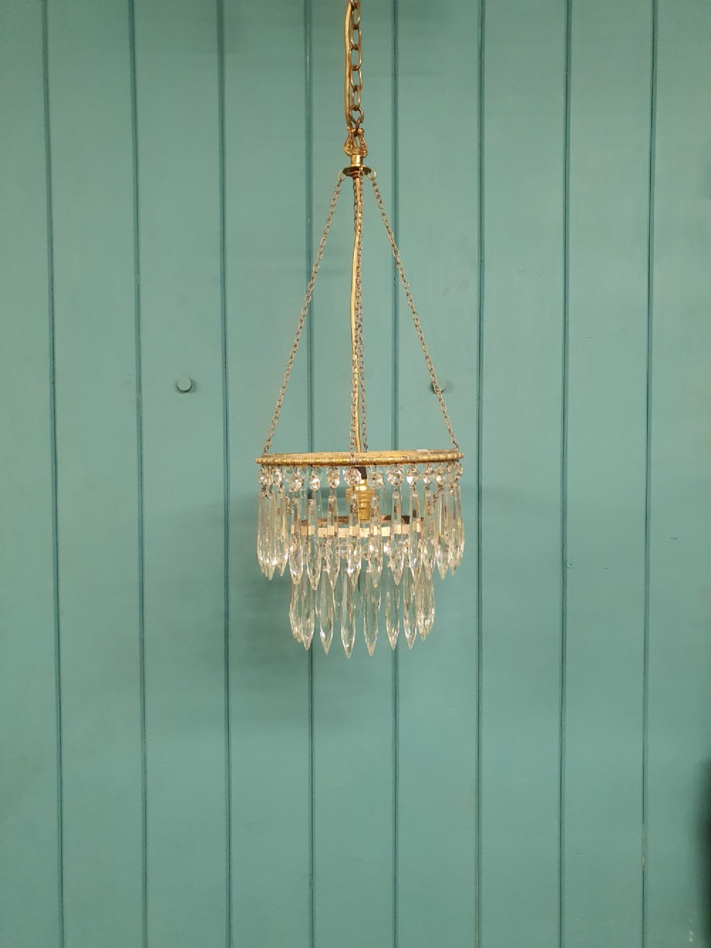 A small early 20th-century pendant chandelier featuring tiered cut-glass crystal spikes suspended from a brass circular frame and hanging chain.