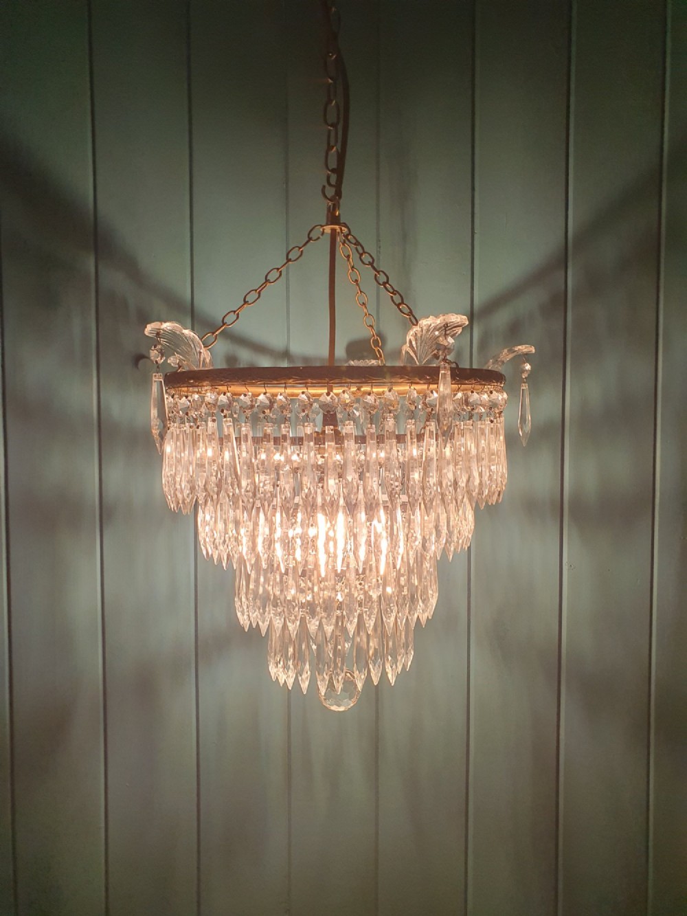 An early twentieth-century four-tiered chandelier featuring hanging glass crystal spikes suspended from a decorated brass rim with chain hanging apparatus. View II