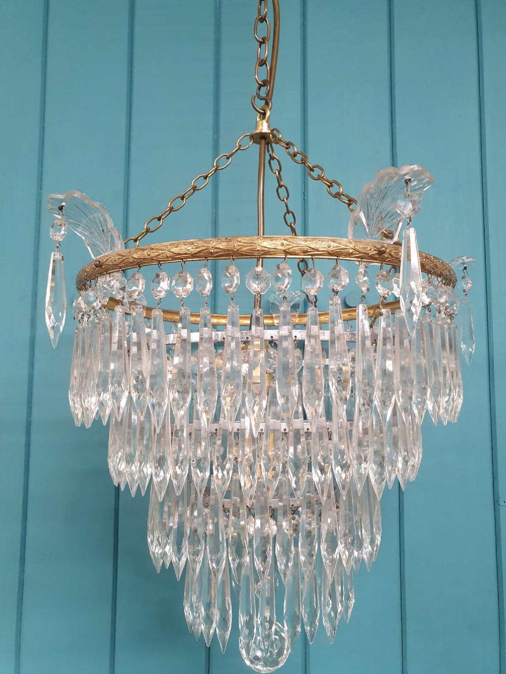 An early twentieth-century four-tiered chandelier featuring hanging glass crystal spikes suspended from a decorated brass rim with chain hanging apparatus. View IV