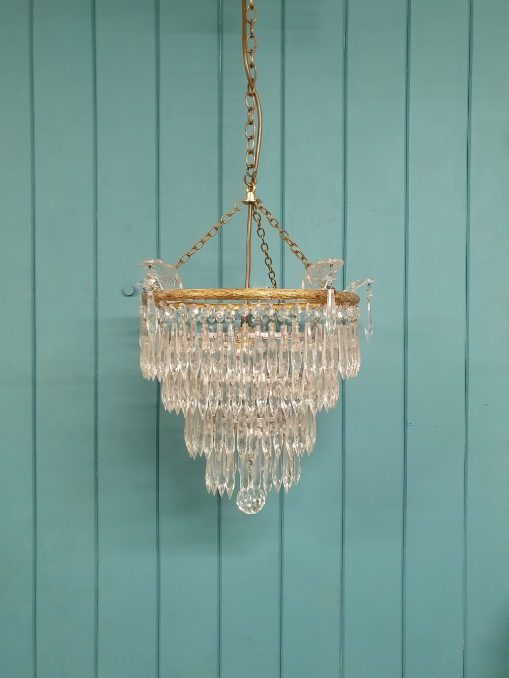 An early twentieth-century four-tiered chandelier featuring hanging glass crystal spikes suspended from a decorated brass rim with chain hanging apparatus.