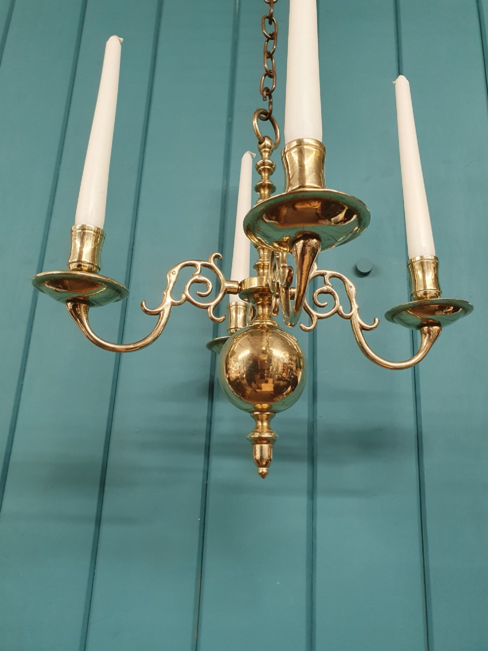A small four-arm brass candle chandelier featuring scroll branches and a central turned column suspended from a brass chain. View II
