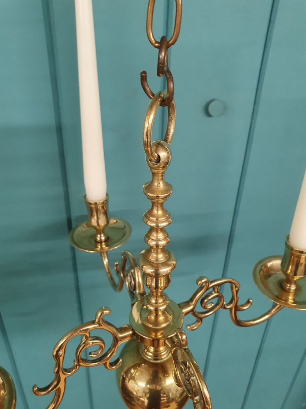 A small four-arm brass candle chandelier featuring scroll branches and a central turned column suspended from a brass chain. View IV