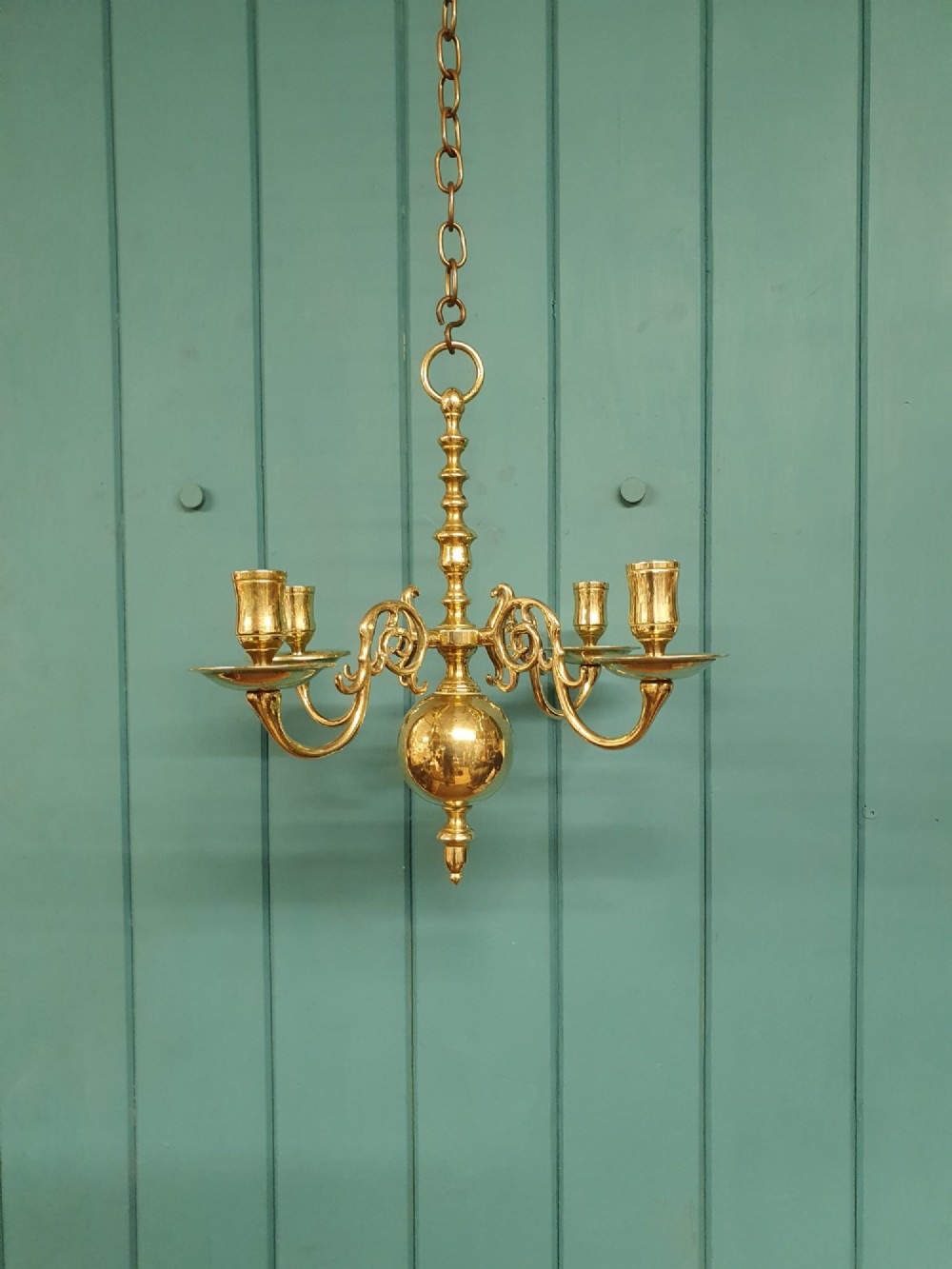 A small four-arm brass candle chandelier featuring scroll branches and a central turned column suspended from a brass chain. View VII