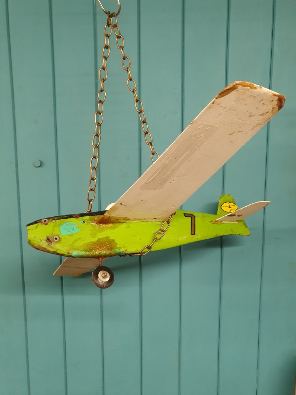 A mid-century hand-painted balsa wood control-line model aeroplane finished in green and cream with number seven painted on the fuselage. View V
