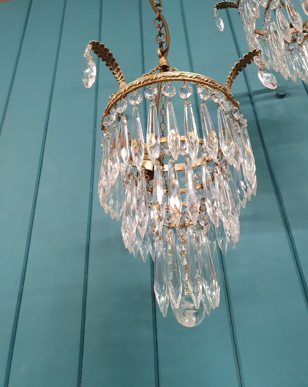 A pair of early 20th-century brass ceiling pendant chandeliers featuring tiered cut crystal spikes and hanging drops. View II