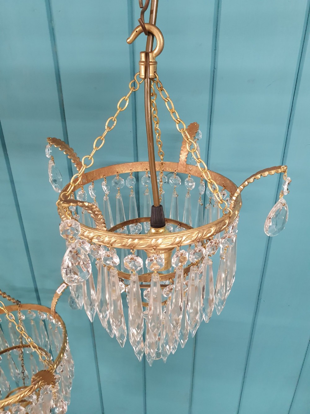 A pair of early 20th-century brass ceiling pendant chandeliers featuring tiered cut crystal spikes and hanging drops. View V