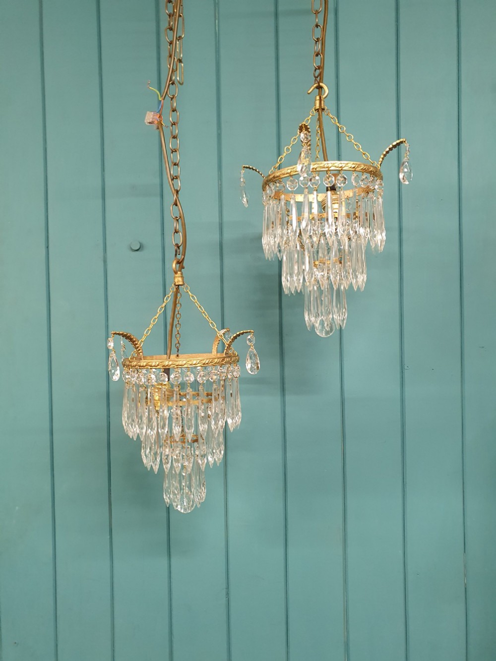 A pair of early 20th-century brass ceiling pendant chandeliers featuring tiered cut crystal spikes and hanging drops.