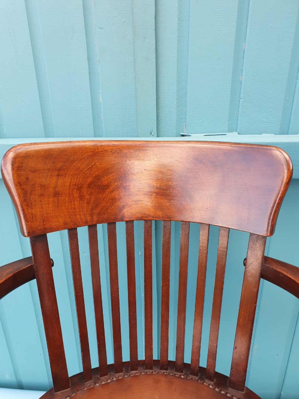 An Edwardian dark wood swivel desk chair with a slatted backrest, curved armrests, a brown leather padded seat, and four splayed legs on castors. View IV