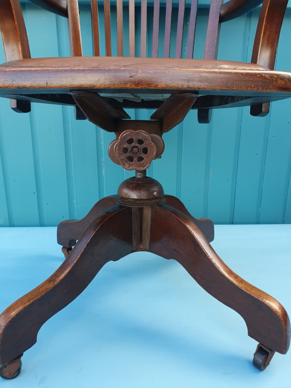 An Edwardian dark wood swivel desk chair with a slatted backrest, curved armrests, a brown leather padded seat, and four splayed legs on castors. View VI