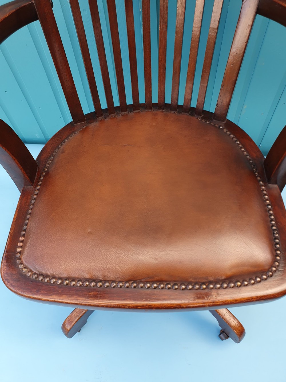 An Edwardian dark wood swivel desk chair with a slatted backrest, curved armrests, a brown leather padded seat, and four splayed legs on castors. View VIII
