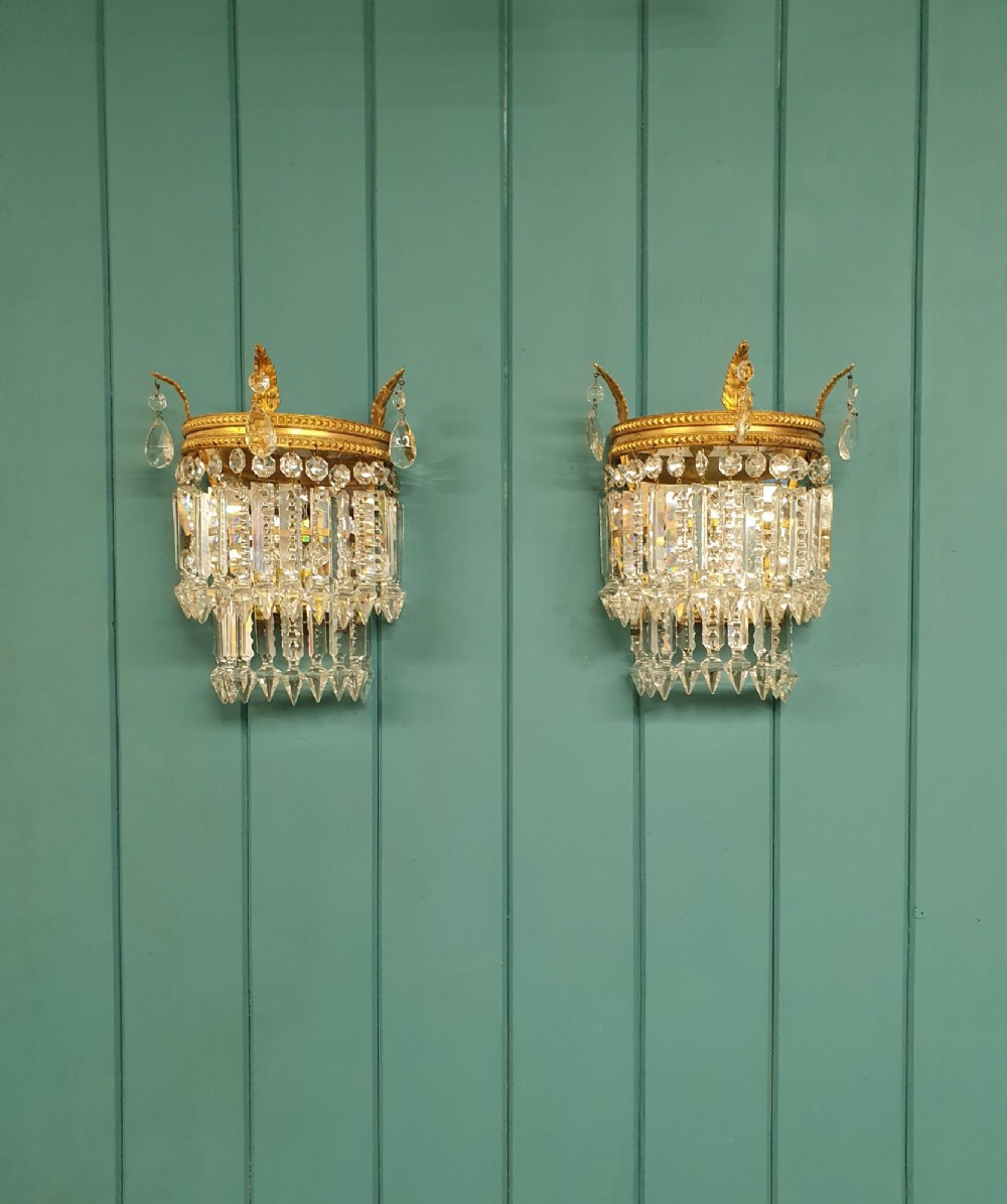 A pair of antique gilt brass wall lights with cascading tiers of cut glass crystal prisms.