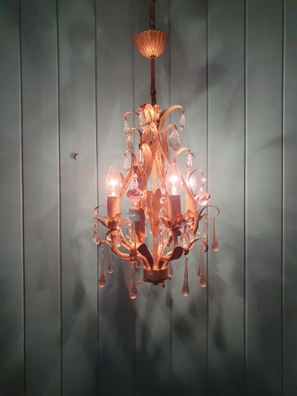 An early 20th-century French gilt metal three-arm chandelier adorned with clear crystal drops and pink glass flower accents. View V