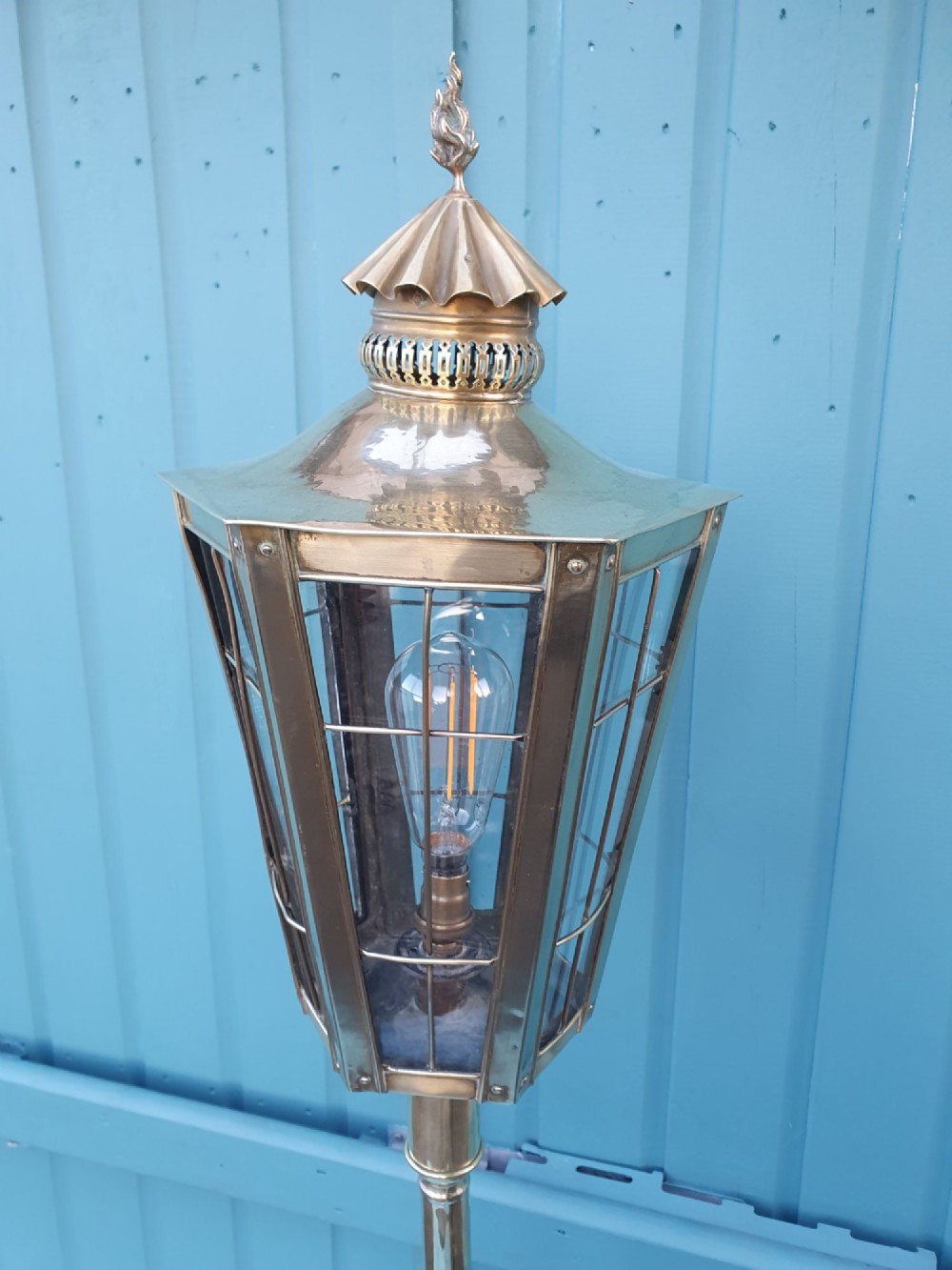 A tall, polished brass floor-standing lantern lamp featuring a hexagonal glass enclosure mounted on a slender turned stem and a circular stepped base with paw feet. View III