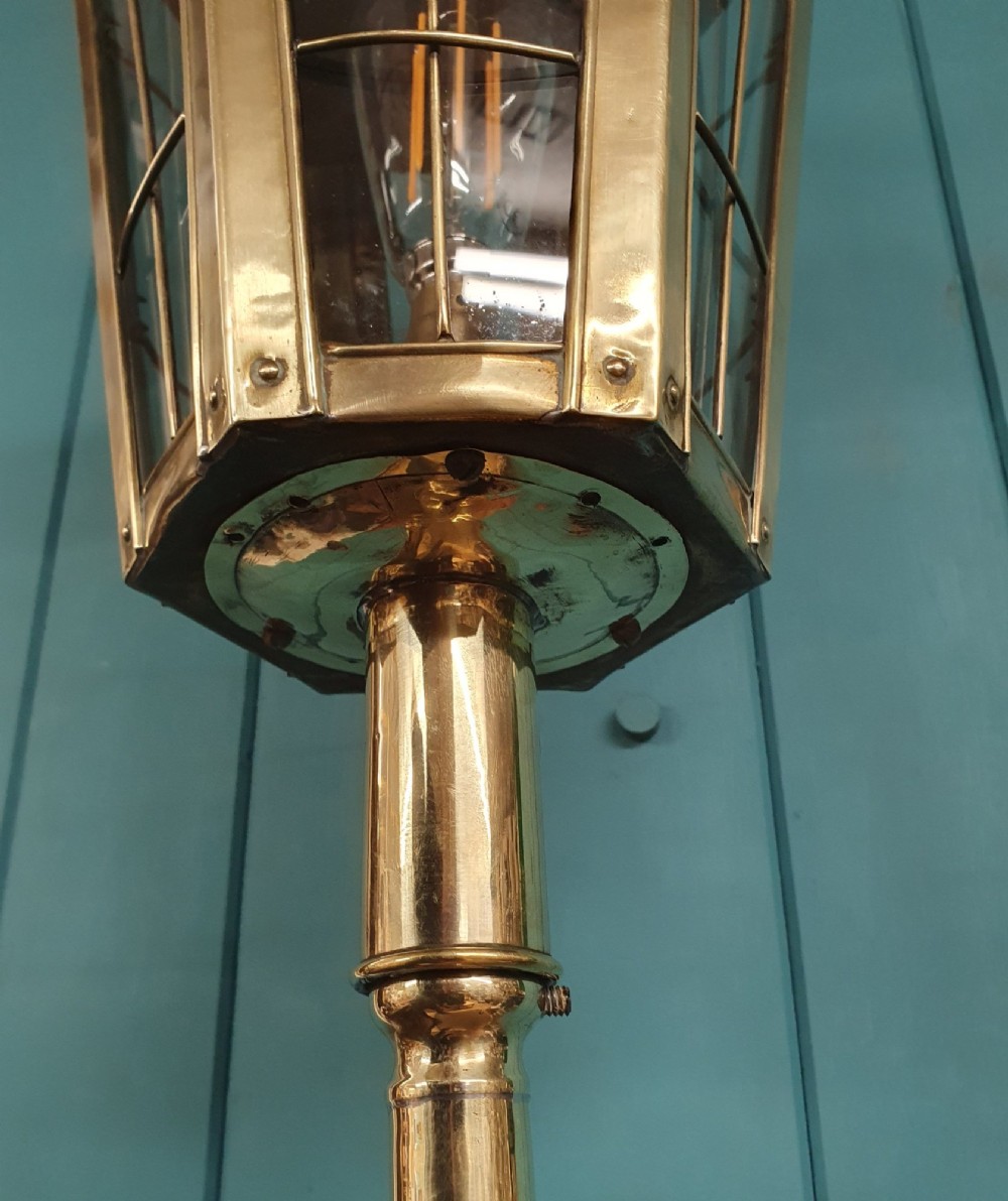 A tall, polished brass floor-standing lantern lamp featuring a hexagonal glass enclosure mounted on a slender turned stem and a circular stepped base with paw feet. View VII