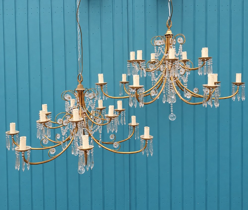 A pair of brass two-tier fourteen-arm chandeliers adorned with cut glass crystal droplets and faux candle light sockets.