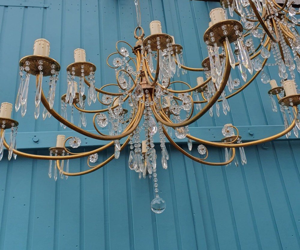 A pair of brass two-tier fourteen-arm chandeliers adorned with cut glass crystal droplets and faux candle light sockets. View III