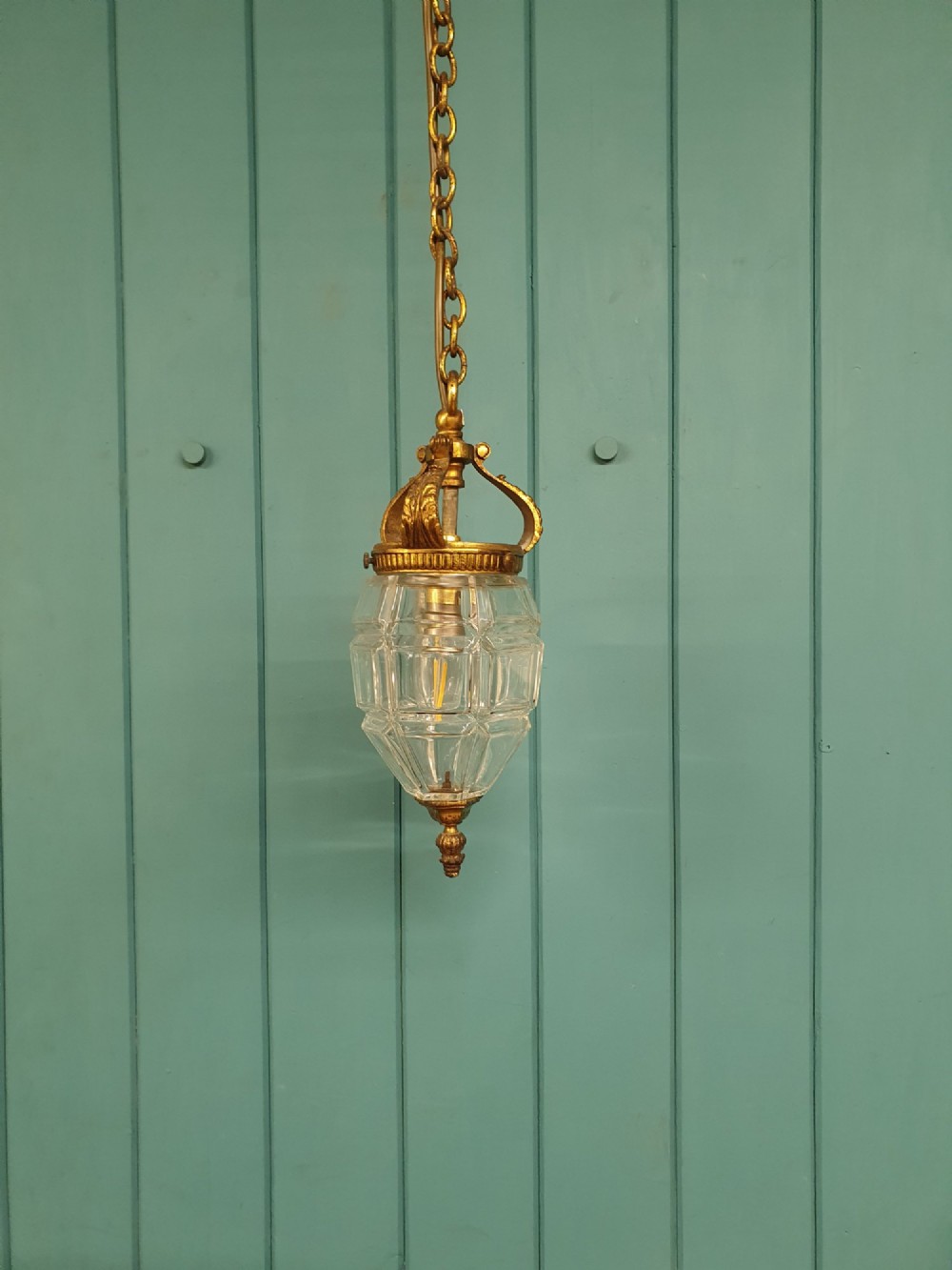 An antique French hanging lantern made of faceted moulded clear glass with an ornate brass crown mount, bottom finial, and suspension chain.