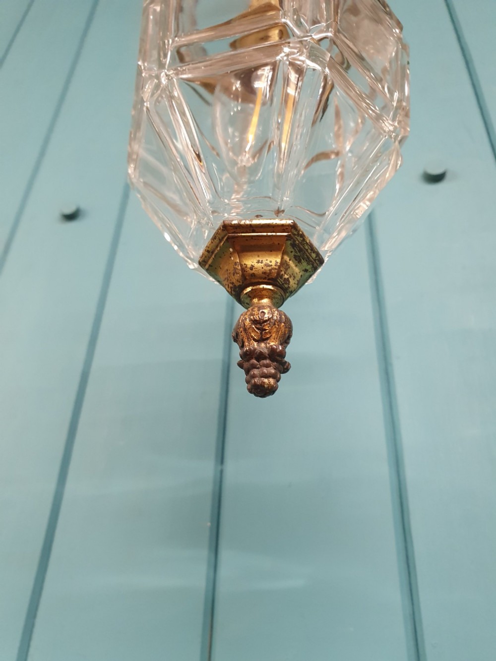 An antique French hanging lantern made of faceted moulded clear glass with an ornate brass crown mount, bottom finial, and suspension chain. View II