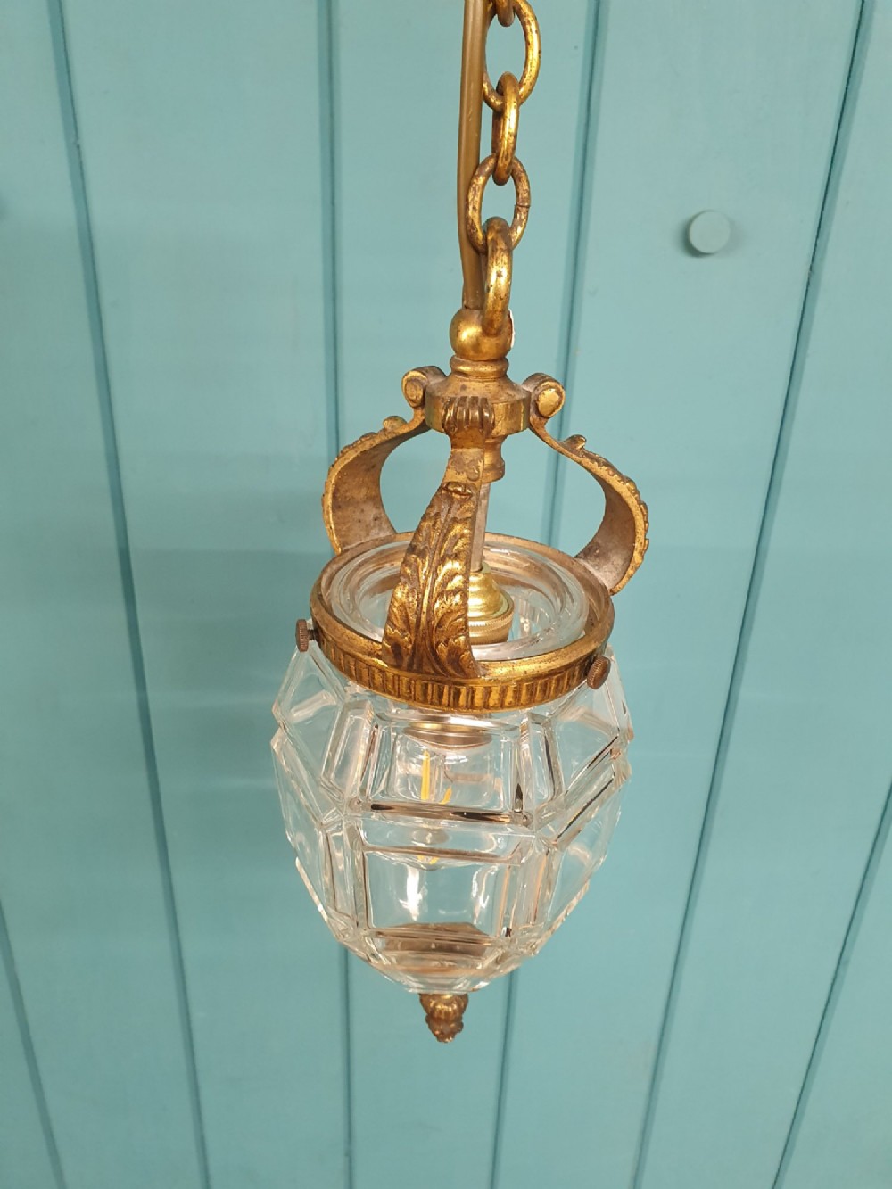 An antique French hanging lantern made of faceted moulded clear glass with an ornate brass crown mount, bottom finial, and suspension chain. View III