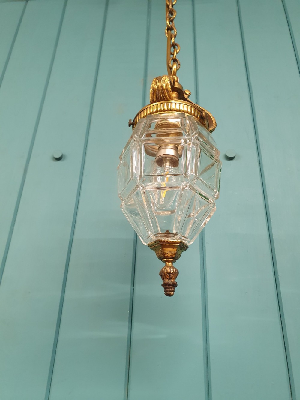 An antique French hanging lantern made of faceted moulded clear glass with an ornate brass crown mount, bottom finial, and suspension chain. View IV