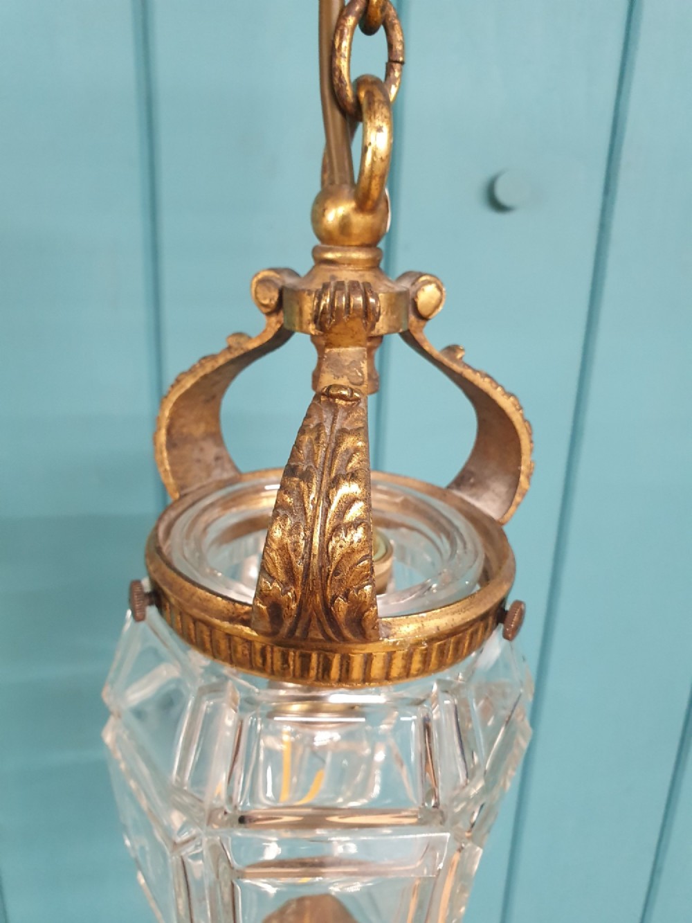 An antique French hanging lantern made of faceted moulded clear glass with an ornate brass crown mount, bottom finial, and suspension chain. View V