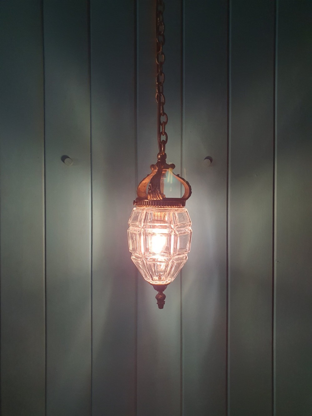 An antique French hanging lantern made of faceted moulded clear glass with an ornate brass crown mount, bottom finial, and suspension chain. View VI