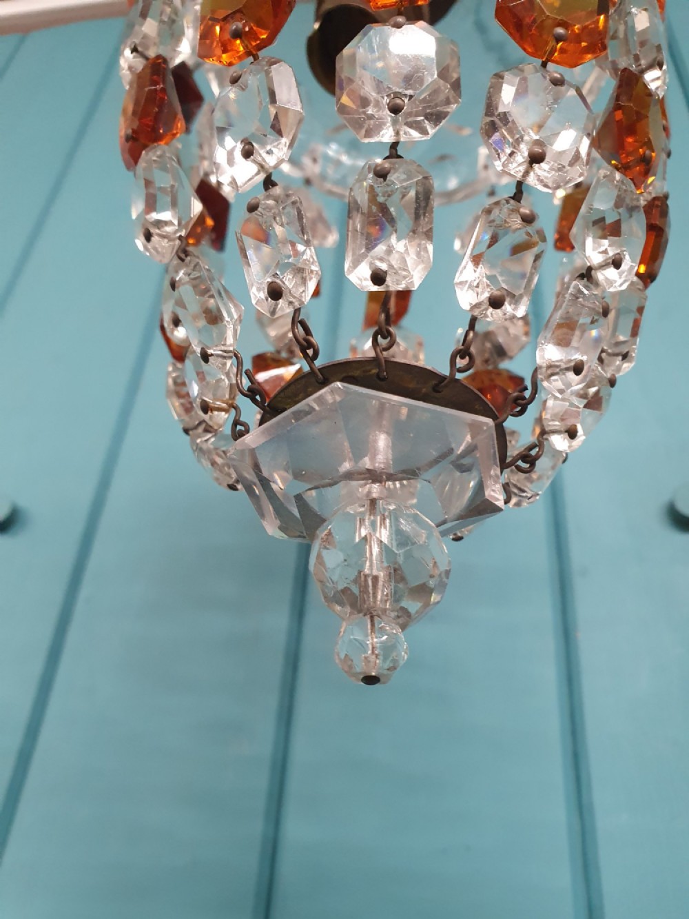 An early 20th-century bag chandelier with clear and amber faceted crystal beads hanging from a brass chain against a green wooden panelled background. View III