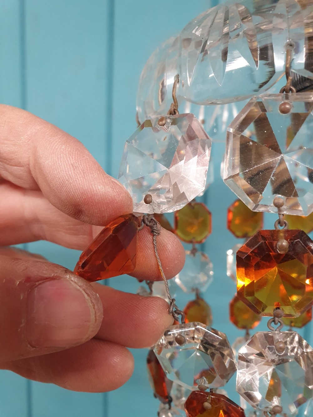 An early 20th-century bag chandelier with clear and amber faceted crystal beads hanging from a brass chain against a green wooden panelled background. View IV