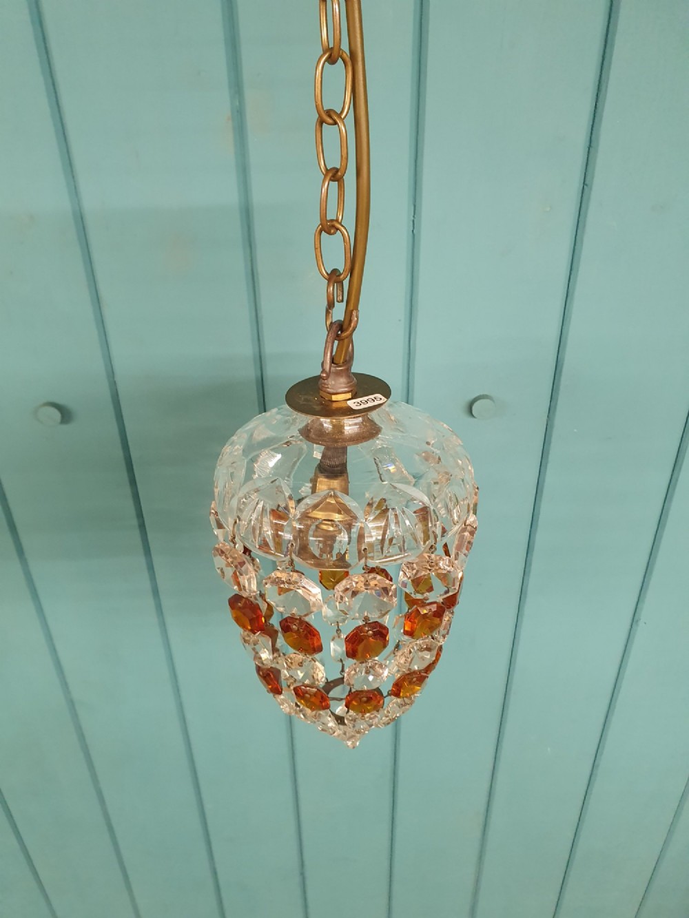 An early 20th-century bag chandelier with clear and amber faceted crystal beads hanging from a brass chain against a green wooden panelled background. View V