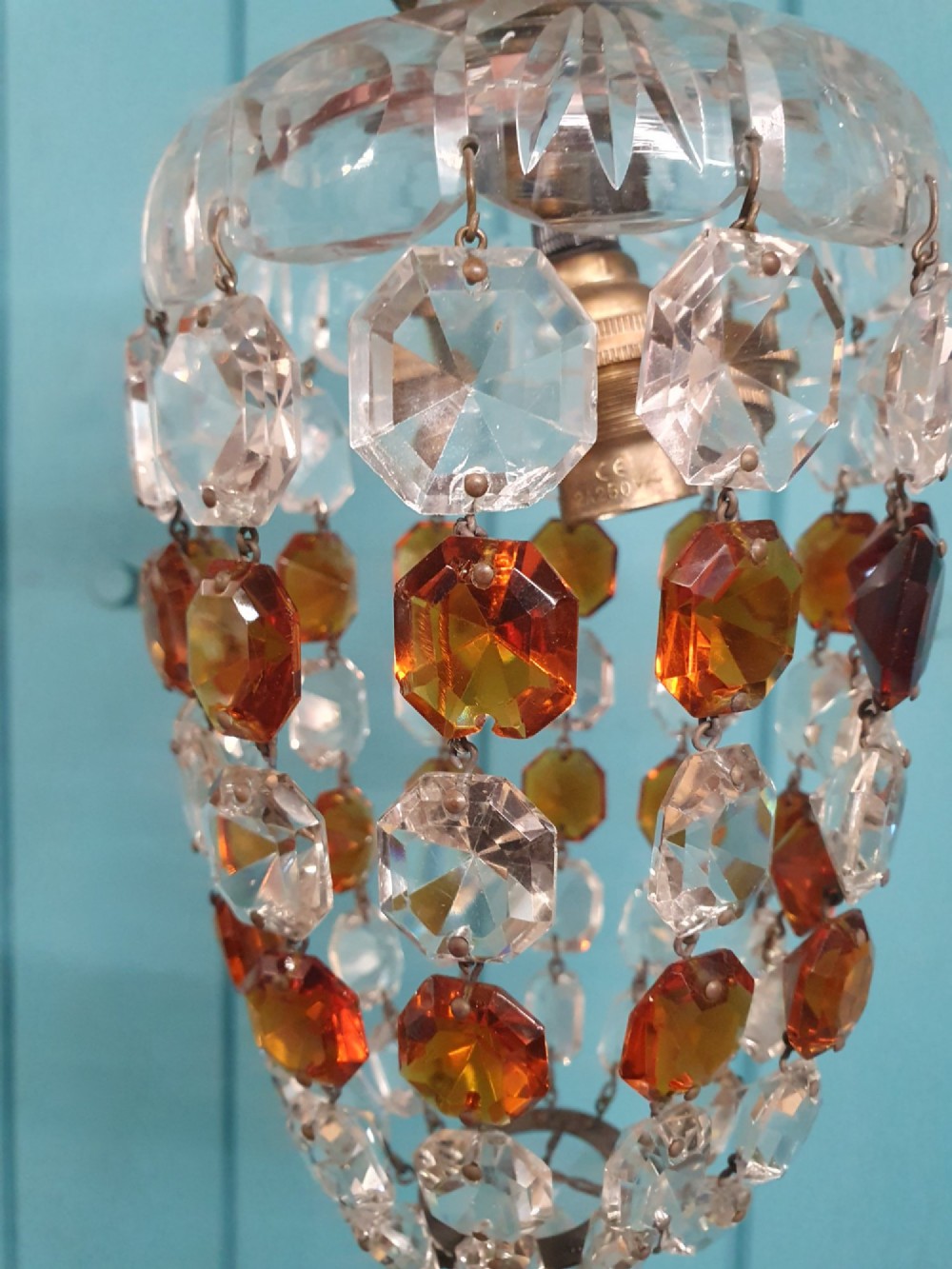 An early 20th-century bag chandelier with clear and amber faceted crystal beads hanging from a brass chain against a green wooden panelled background. View VII