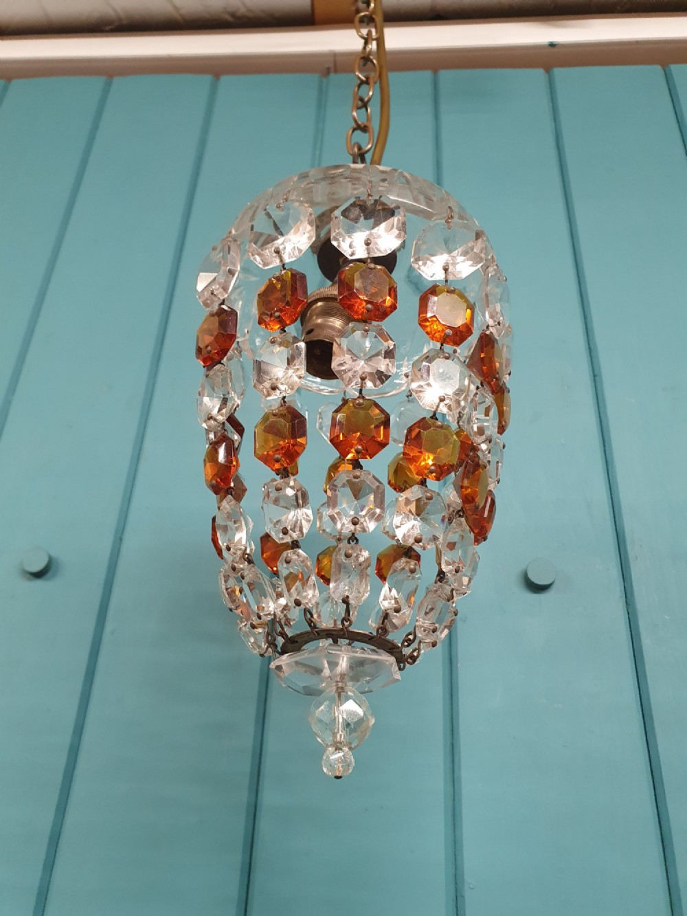 An early 20th-century bag chandelier with clear and amber faceted crystal beads hanging from a brass chain against a green wooden panelled background. View VIII