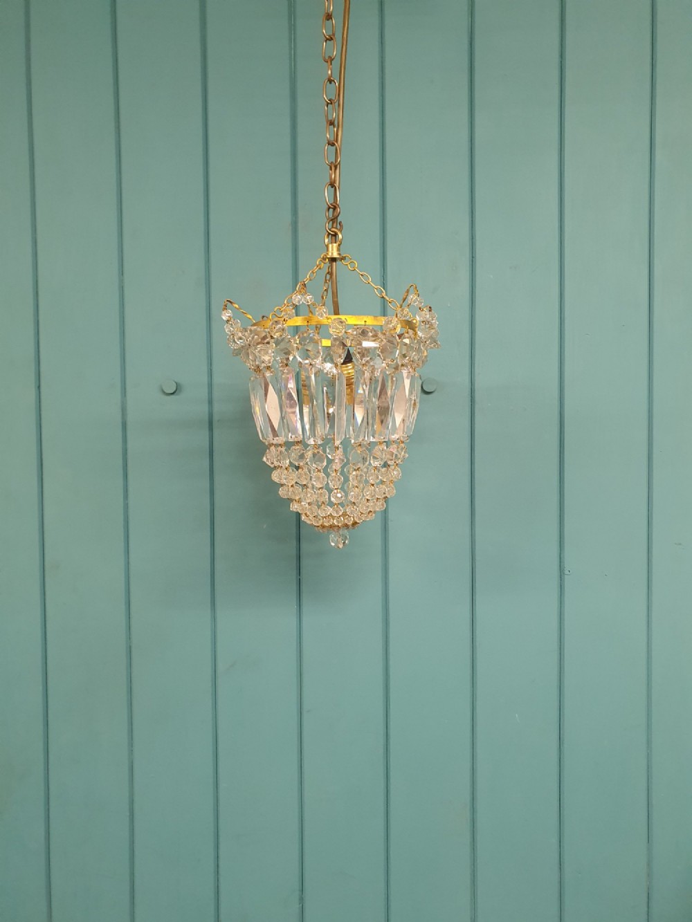 An early 20th-century gilt brass and crystal bag chandelier suspended by a link chain, featuring cascading faceted prisms and glass bead strands.