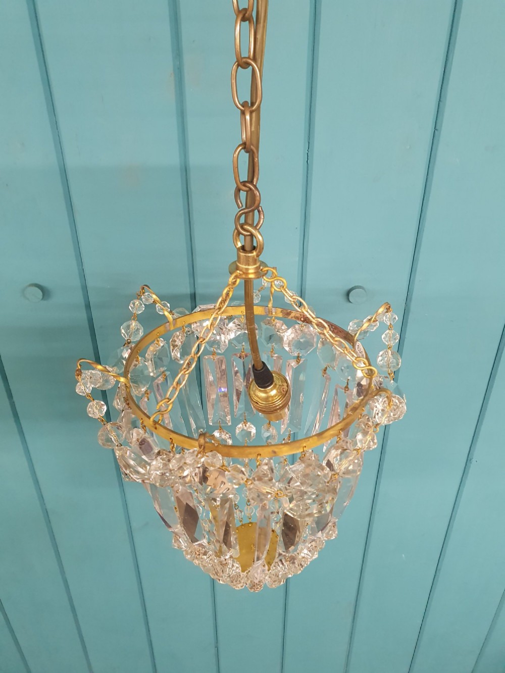 An early 20th-century gilt brass and crystal bag chandelier suspended by a link chain, featuring cascading faceted prisms and glass bead strands. View V
