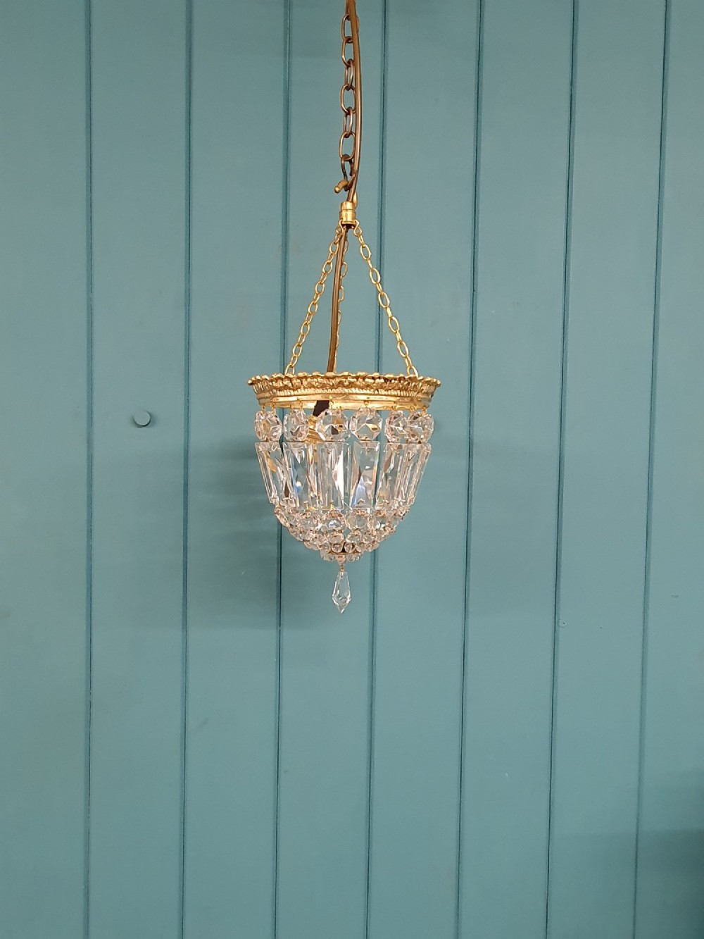 An early twentieth-century gilt brass crystal basket chandelier featuring faceted glass prisms and a suspended chain hanger.