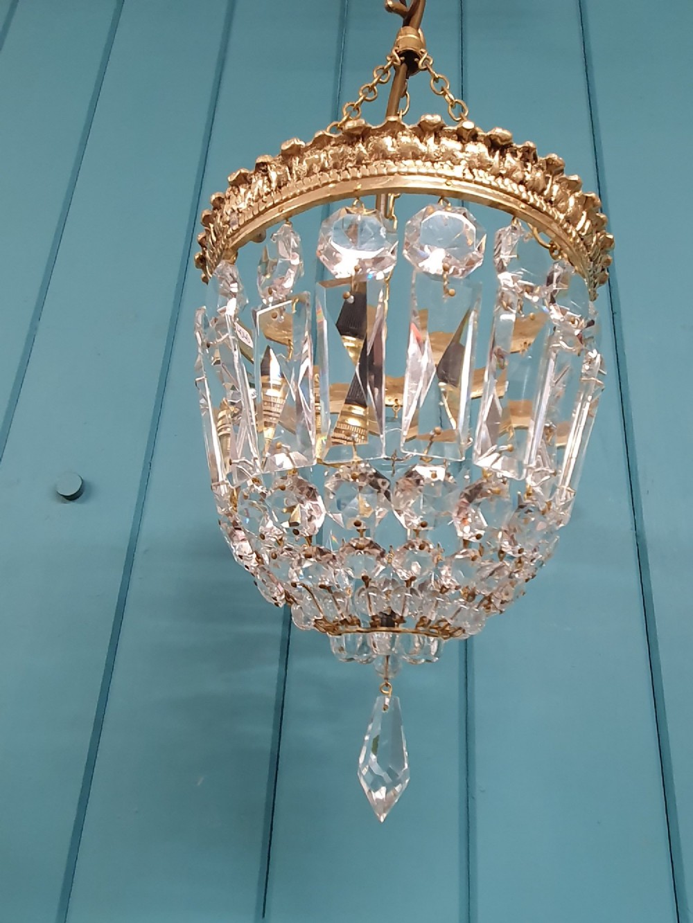 An early twentieth-century gilt brass crystal basket chandelier featuring faceted glass prisms and a suspended chain hanger. View V