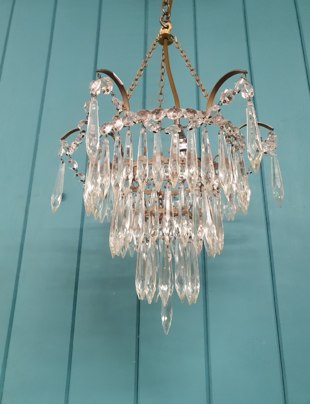 An early 20th century brass light fitting featuring cascading tiers of cut glass crystal teardrops suspended from brass chains. View IV