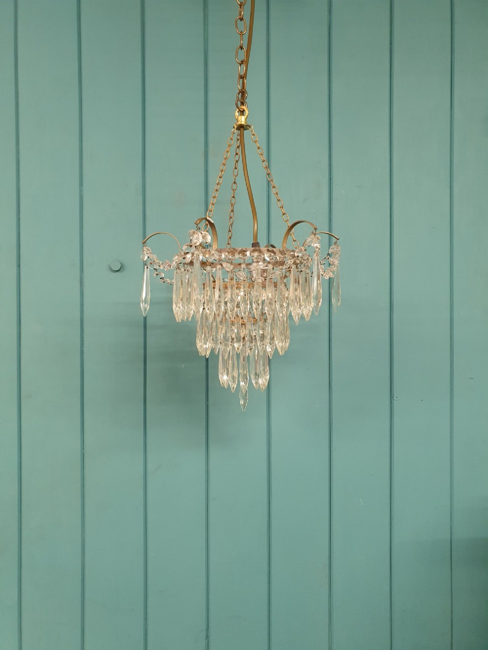 An early 20th century brass light fitting featuring cascading tiers of cut glass crystal teardrops suspended from brass chains.