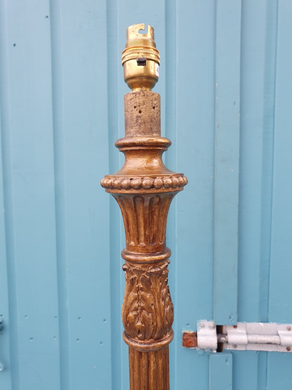 A tall antique carved giltwood standard lamp featuring a fluted column and triform base set against a blue panelled wall. View III