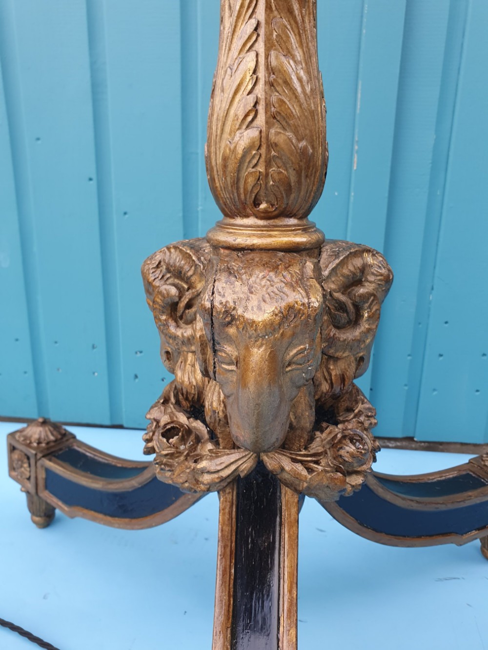 A tall antique carved giltwood standard lamp featuring a fluted column and triform base set against a blue panelled wall. View V