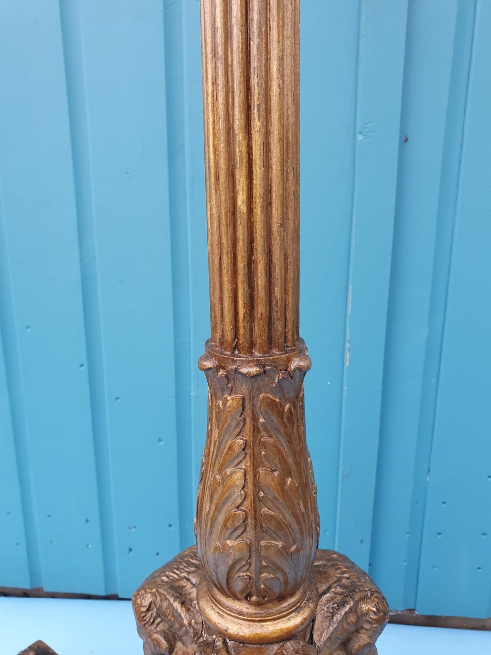 A tall antique carved giltwood standard lamp featuring a fluted column and triform base set against a blue panelled wall. View VIII