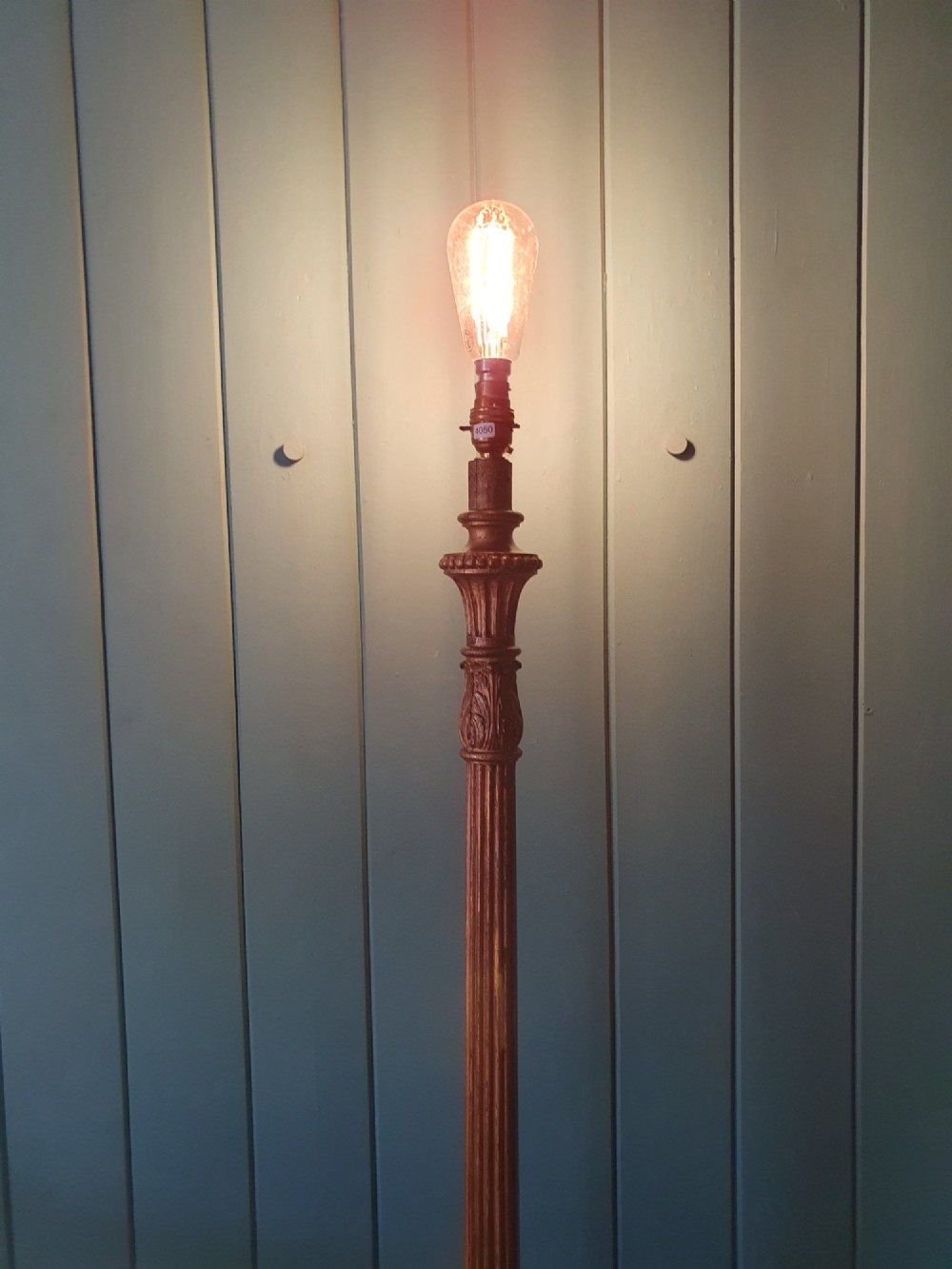 A tall antique carved giltwood standard lamp featuring a fluted column and triform base set against a blue panelled wall. View IX