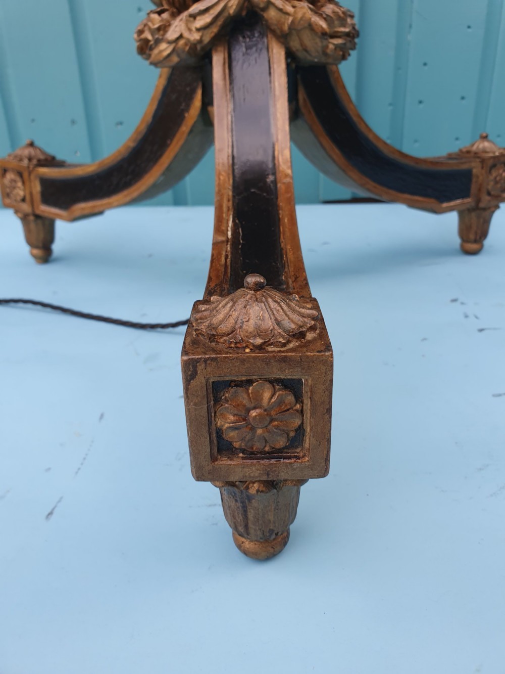 A tall antique carved giltwood standard lamp featuring a fluted column and triform base set against a blue panelled wall. View X