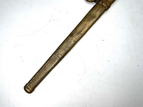 A German Kriegsmarine officer dress dagger featuring a cream wire-wrapped grip, spherical eagle pommel, crossguard, and an engraved brass scabbard with two suspension rings. View III
