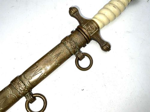 A German Kriegsmarine officer dress dagger featuring a cream wire-wrapped grip, spherical eagle pommel, crossguard, and an engraved brass scabbard with two suspension rings. View V