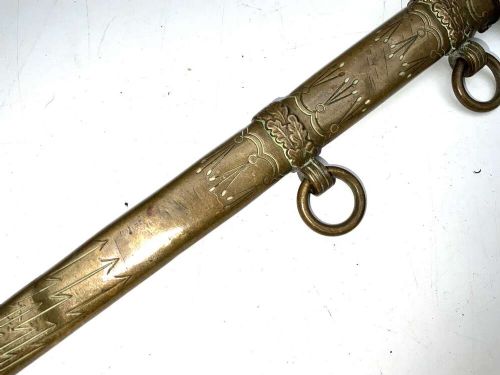 A German Kriegsmarine officer dress dagger featuring a cream wire-wrapped grip, spherical eagle pommel, crossguard, and an engraved brass scabbard with two suspension rings. View VI