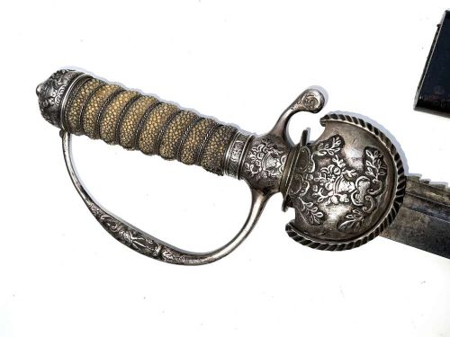 An early 18th-century short sword featuring a silvered hilt and ribbed grip, displayed alongside its black leather scabbard. View IX