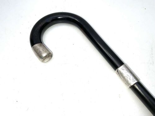 A black ebonised wooden walking stick featuring a curved crook handle, a silver-toned metal collar, and a protective tip. View II